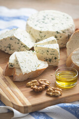 Variety of home made cheese and herbs, olive oil, and bread on a wooden board. Brined curd white cheese with vegetables on the table
