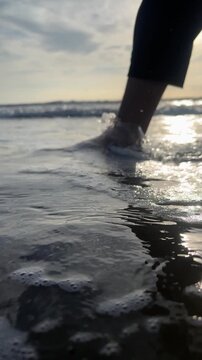 A person's foot is in the water at the beach. The water is calm and the sun is shining on the surface