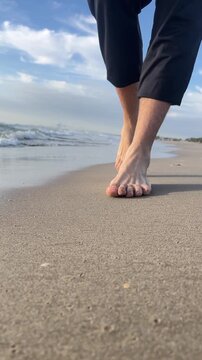 A person is walking on the beach barefoot. The beach is sandy and the sky is cloudy