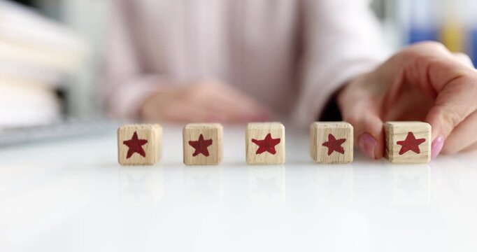 Woman carefully arranges wooden cubes with painted stars in neat row on table. Female aligns star-decorated blocks with precision showing rating