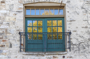 An older exterior wooden multi-paned door and transom window Romeo and Juliet balcony, set in an old limestone building, a wrought iron railing, reflection of tree in windows, nobody