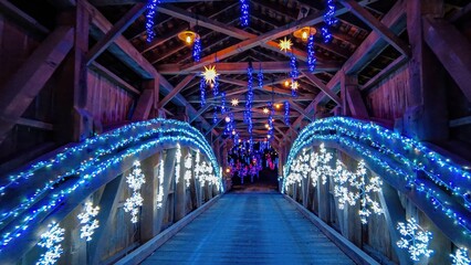 Visitors cross a beautiful wooden bridge adorned with vibrant blue lights and snowflake...