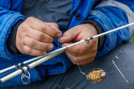 A man is holding a fishing rod and is tying a hook to it