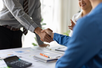 Business partners shaking hands after successful agreement with colleagues clapping hands in background, celebrating business success at meeting.