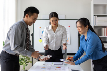 Asian businesspeople are examining documents and charts while discussing business performance during a productive meeting in office.