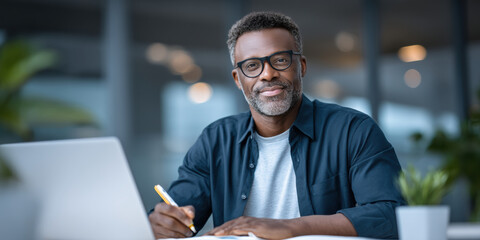 Small business owner smiling at desk with laptop pen and paperwork confident entrepreneur working in modern office