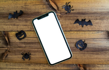 Mockup, smartphone, paper black bat, spiders and pumpkins on wooden background. Halloween background.