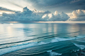 A beautiful summer sunset reflects over the calm blue ocean waves under a vast sky as the sun meets the horizon in this stunning coastal landscape view