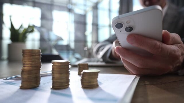 A man is looking at his phone while holding a stack of coins