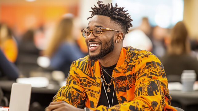 Engaged Black man with dreadlocks and stylish glasses, smiling brightly while attending lively professional or educational event indoors