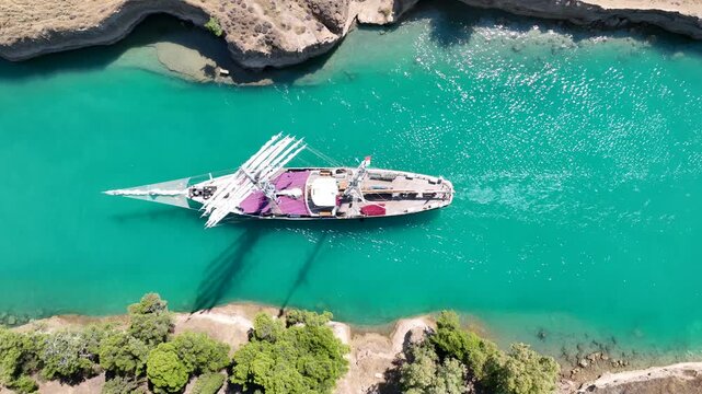 Aerial drone cinematic video of classic sailing boat crossing narrow Corinth canal of Isthmus from West submersible bridge and narrow opening of Corinthian gulf to Saronic gulf, Loutraki, Greece