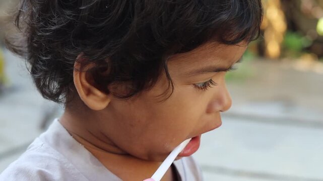 Adorable two-year-old Indian girl brushing her teeth outdoors in the morning, smiling playfully while learning good hygiene habit, selective focus 