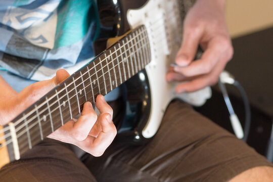 Human hand playing an electric guitar holding a chord with strings using a guitar pick