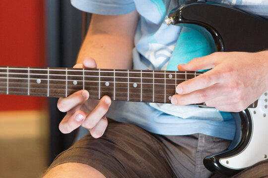 Human hand playing an electric guitar holding a chord with strings using a guitar pick