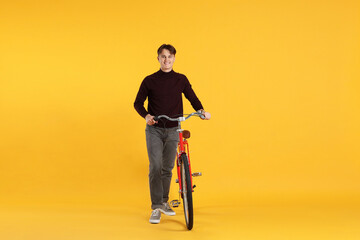 Fototapeta premium Handsome man with red bicycle on orange background
