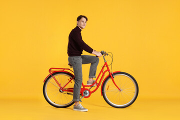 Fototapeta premium Handsome man riding red bicycle on orange background