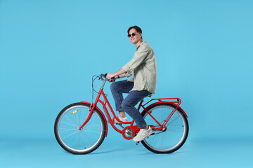 Obraz premium Handsome man riding red bicycle on light blue background