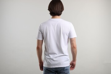 Obraz premium Young man wearing stylish white t-shirt near light grey background, back view. Mockup for design