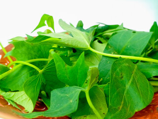 Sweet potato leaves on a brown plate, isolated on white background.