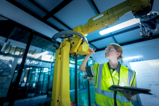 A robotics engineer uses a tablet to program a robot with a machine vision system, while her colleague calibrates the end-of-arm tooling on another unit in a system integration lab.