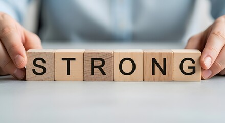 Obraz premium Hands arranging wooden blocks spelling the word strong
