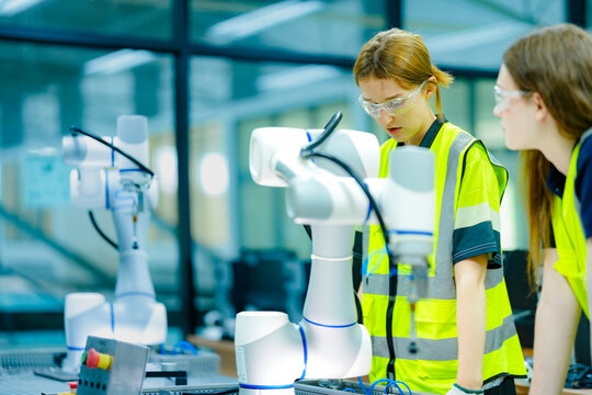 Two female engineering students in a high-tech university lab collaborate on a robotics project, learning hands-on programming skills for the future of industrial automation.