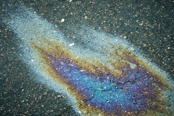 Oil slick on wet asphalt showing vibrant iridescent colors and pollution concept.