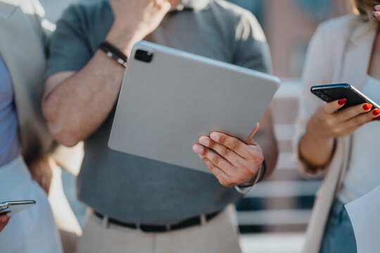 Group of people engages in business discussion using modern devices on a rooftop setting. Dynamic sunset lighting emphasizes a collaborative and productive atmosphere.