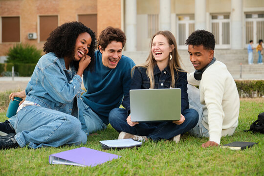 Happy diverse students enjoying campus life while watching a laptop and laughing