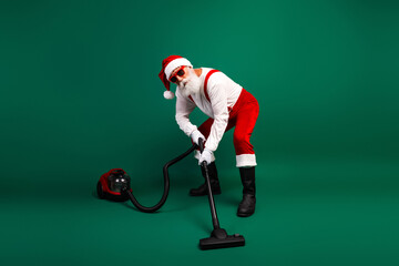 Santa Claus vacuuming with a funny pose in a cool Christmas costume against a green background