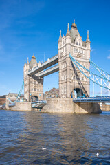 Obraz premium Tower Bridge stands majestically over the River Thames on a clear day, showcasing its iconic architecture and blue suspension cables. Boaters can be seen navigating the waters below.