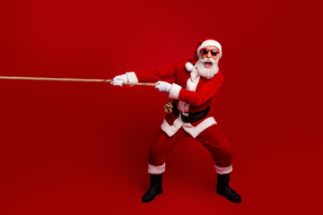 Santa Claus pulling a rope in a festive pose wearing sunglass on a vibrant red background