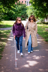Visually impaired woman walking with her female friend in the city park