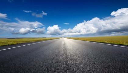 empty asphalt road stretches under a vibrant blue sky dotted with fluffy white clouds