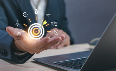 Businessman hand holding virtual target icon with dartboard and marketing strategy symbol, concept of goal setting, business success, KPI management, and performance optimization