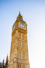 Obraz premium Big Ben, a famous clock tower in London, showcases its intricate architecture. The sky is clear, and the structure reflects sunlight, highlighting its iconic features.