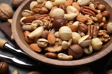 Mix of different nuts in bowl and nutcracker on table, closeup