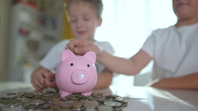 Children saving money in piggybank at home. Children learning about banks by filling piggybank with coins. Concept of early financial education. Children using piggybank at home as their first bank.
