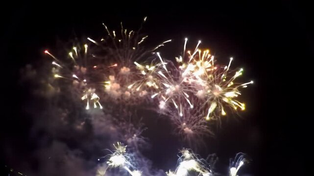 Establishing wide video of vibrant, exploding gold, red, blue, green, purple fireworks against inky black night sky. Dolly into grand pyrotechnic festive spectacle