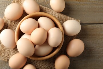 Raw chicken eggs in bowl on wooden table, flat lay