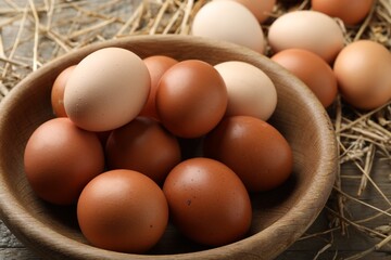 Raw chicken eggs in bowl and straw on wooden table, closeup