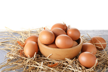 Raw chicken eggs, feathers, bowl and straw on grey wooden table against white background