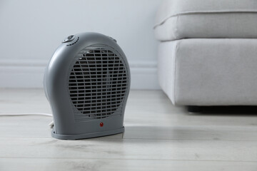 Electric fan heater on light wooden floor indoors, closeup. Space for text