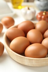 Raw chicken eggs in bowl on white table, closeup