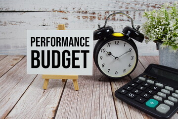 Performance Budget text with alarm clock and calculator on wooden background