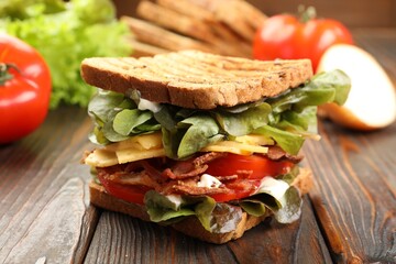 Tasty sandwich with bacon, cheese, vegetables and sauce on wooden table, closeup
