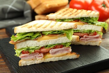 Tasty sandwiches with ham, bacon, cheese and vegetables on wooden table, closeup