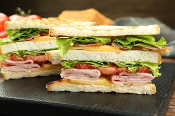 Tasty sandwiches with ham, bacon, cheese and vegetables on black wooden board, closeup