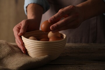 Man putting raw chicken egg into bowl at wooden table, closeup