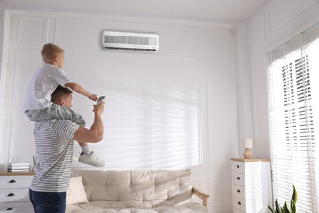 Father and son switching on air conditioner with remote control at home